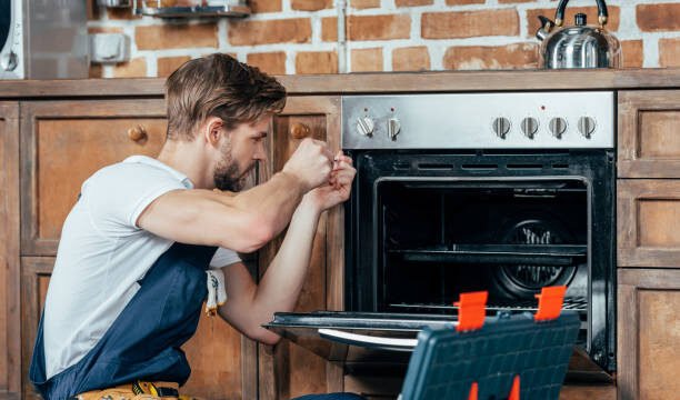 young repairman in protective workwear fixing oven in kitchen