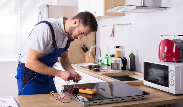 Male Technician Repairing Induction Stove With Digital Multimeter In Kitchen