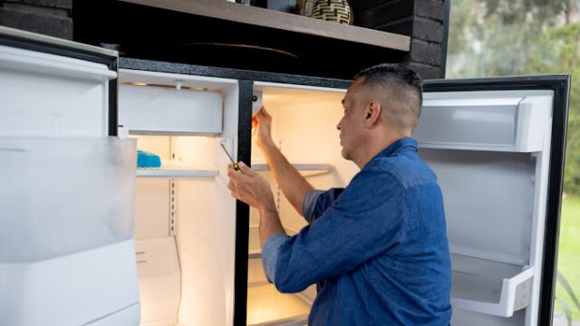 Latin American handyman fixing a fridge at a house – domestic life concepts